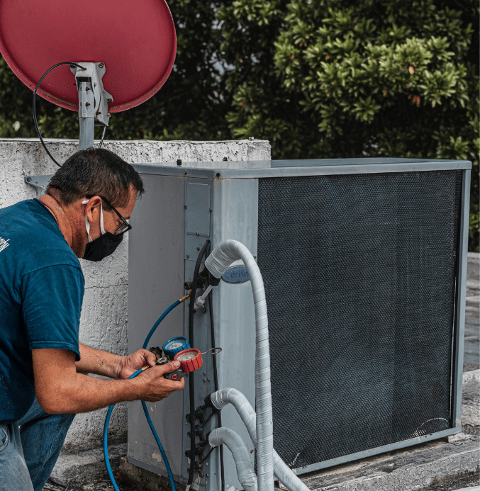 Technician using a manifold gauge set to measure refrigerant pressure during air conditioning system maintenance.