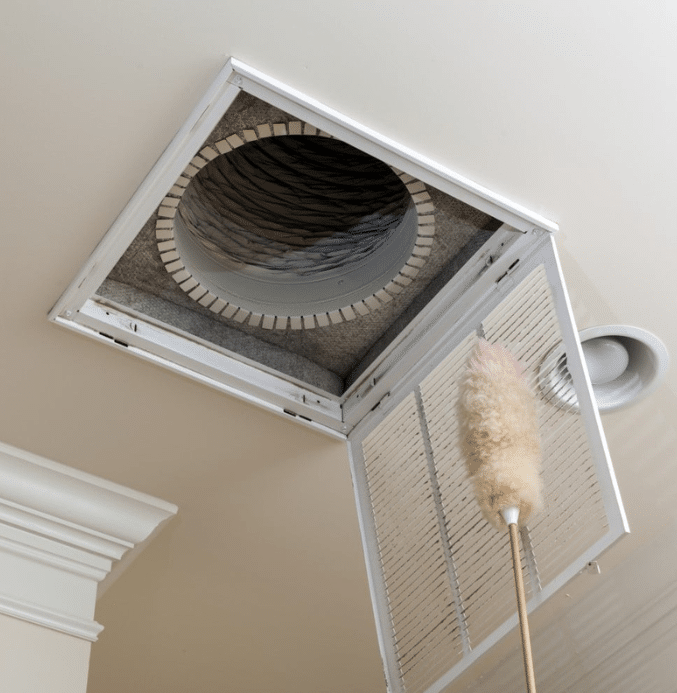 Open ceiling air vent being cleaned with a duster as part of residential HVAC duct cleaning and maintenance.